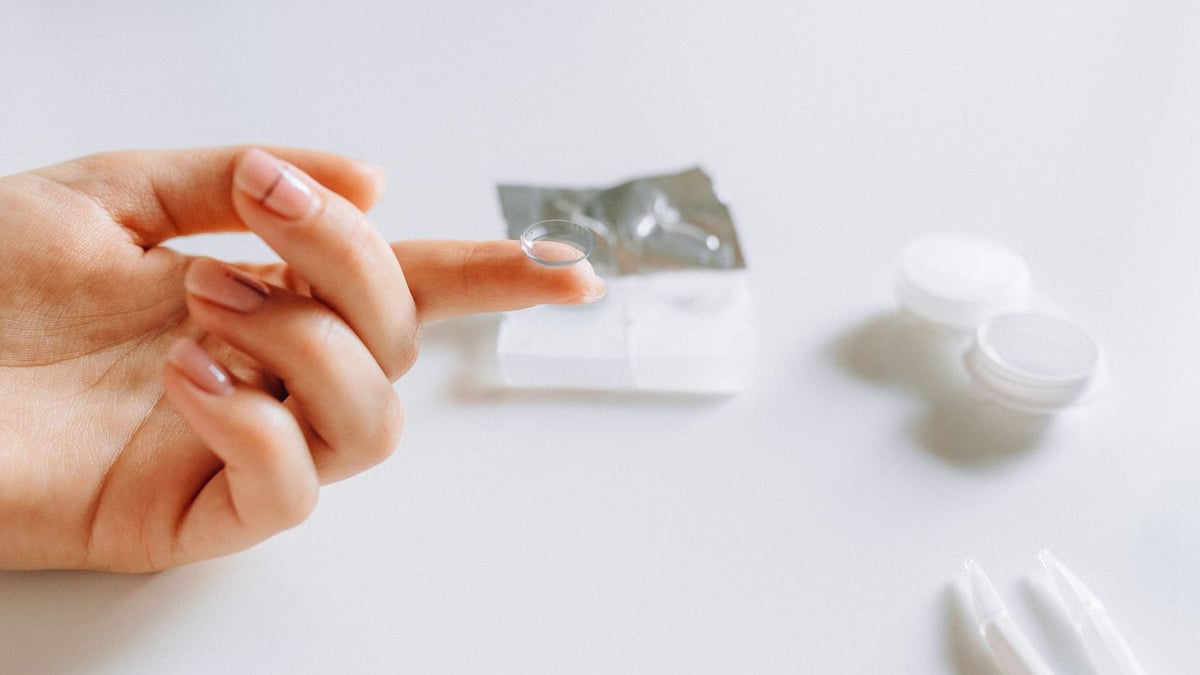A contact lens balanced on a fingertip - wearing contacts with eyelash extensions