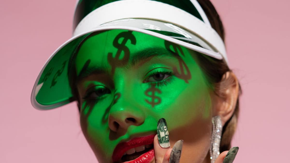 Dollar-sign shadows across a woman's face with a dollar-bill manicure - the cost of beauty in NYC
