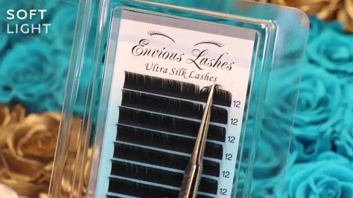 Envious Lashes ultra silk lash tray with tweezers lifting a strand, on gold and teal roses